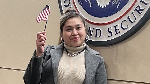 Jocelyn waves an american flag. On the wall behind is the US Department of Homeland Security seal.